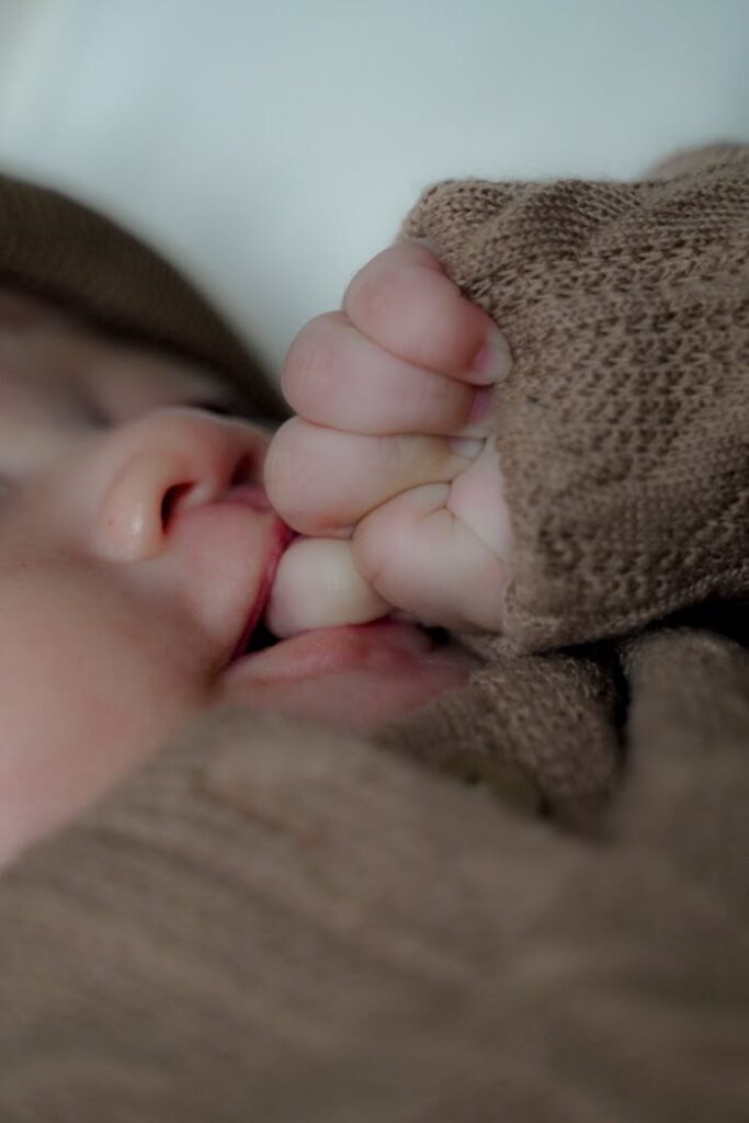 Adorable baby sucking thumb, wrapped in a cozy brown blanket. Perfect for warmth and comfort themes.